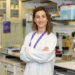A female researcher wearing a lab coat with her arm folded facing the camera