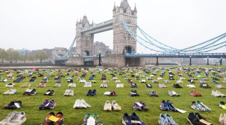 Rows of trainers with dedications attached to the laces set out on the grass with Tower Bridge in the background